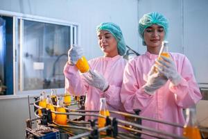 asiatische arbeiterin überprüft produktflaschen mit fruchtsaft auf der produktionslinie in der getränkefabrik. Hersteller prüft Qualität der Lebensmittelindustrie. foto