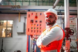 professioneller ingenieur mit helmarbeiten zur wartung von industriebaugeräten. Arbeiter stehen mit verschränkten Armen in der Fabrik. foto