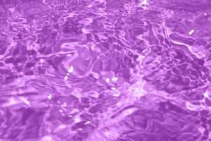 defocus verschwommene transparente lila gefärbte klare ruhige wasseroberflächenstruktur mit spritzer, blase. glänzender lila wasserkräuselungshintergrund. Wasseroberfläche im Schwimmbad. lila Blasenwasser glänzt. foto