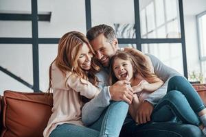 glückliche junge familie, die lächelt und sich umarmt, während sie sich zu hause verbindet foto