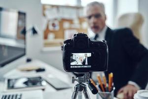 Senior Mann im eleganten Business-Anzug mit modernen Technologien beim Erstellen von Social-Media-Videos foto