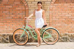 Schönheit mit Oldtimer-Fahrrad. volle Länge der attraktiven jungen lächelnden Frau, die nahe ihrem Weinlesefahrrad steht foto