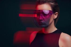 Selbstbewusste junge Frau mit futuristischer Brille vor dunklem Hintergrund foto
