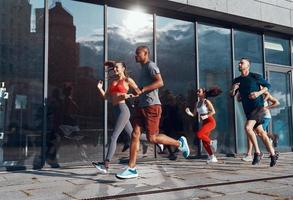 Volle Länge von jungen Menschen in Sportkleidung, die beim Training auf dem Bürgersteig im Freien joggen foto