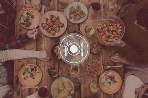 Essen ist angerichtet. Digital komponiertes Bild von Küchenutensilien über Draufsicht von vier Personen, die zusammen zu Abend essen, während sie am rustikalen Holztisch sitzen foto