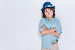 voller Inspiration. kleiner Junge, der Hut trägt und die Arme verschränkt hält, während er vor weißem Hintergrund steht foto