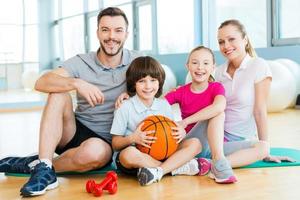 glücklich, eine Familie zu sein. Fröhliche sportliche Familie, die sich beim gemeinsamen Sitzen auf der Trainingsmatte miteinander verbindet foto