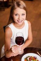 mit Wein anstoßen. Blick von oben auf die schöne junge Frau, die mit Rotwein röstet und lächelt, während sie im Restaurant sitzt foto