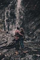 die Schönheit der Natur genießen. Rückansicht in voller Länge eines jungen Paares, das sich umarmt, während es in der Nähe des Wasserfalls steht foto