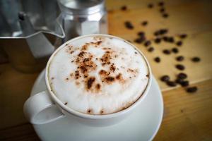 Heißer Cappuccino in weißer Tasse mit Holzhintergrund, Kaffee ist ein beliebtes Getränk auf der ganzen Welt. foto