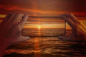 Das Mädchen fotografiert den Sonnenuntergang am Meer auf einem Smartphone. Hände und Smartphone-Nahaufnahme. foto