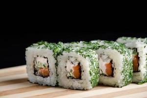 Uramaki-Sushi-Rolle auf Holztablett auf schwarzem Hintergrund. beliebtes asiatisches Gericht.