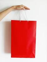 Hand, die rote Einkaufstasche auf weißem Hintergrund hält foto