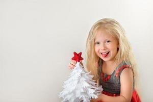 kleines lächelndes mädchen mit weißem papierweihnachtsbaum und rotem stern in ihren händen foto