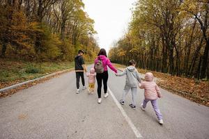 Rücken der Mutter mit vier Kindern, die im Herbstwald auf der Straße laufen. foto