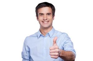 erfolgreicher Geschäftsmann. Porträt eines hübschen jungen Mannes im blauen Hemd, der seinen Daumen nach oben zeigt und lächelt, während er isoliert auf Weiß steht foto
