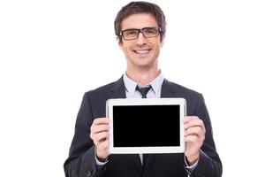 Kopieren Sie Platz auf seinem Tablet. Hübscher junger Mann in Abendkleidung und Brille, der den Monitor seines digitalen Tablets zeigt und lächelt, während er isoliert auf weißem Hintergrund steht foto