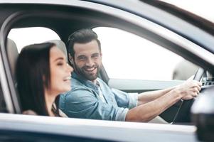die Reise genießen. junges Paar sitzt im Auto und lächelt, während ein gutaussehender Mann die Hände am Lenkrad hält foto