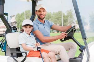 Vater und Sohn im Golfwagen. lächelnder kleiner Junge, der im Golfwagen sitzt, während sein Vater ihn fährt foto