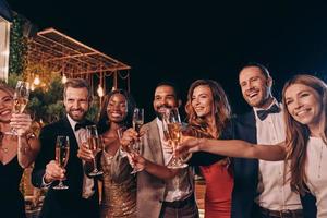 Gruppe von Menschen in formeller Kleidung, die mit Champagner anstoßen und lächeln, während sie Zeit auf einer Luxusparty verbringen foto