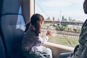 süßes kleines Mädchen, das durch ein Fenster schaut, während es die Zugfahrt genießt foto