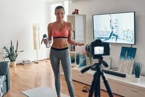 Schöne junge Frau in Sportkleidung, die trainiert und lächelt, während sie Social-Media-Videos macht foto