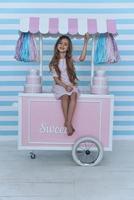 schönes Kind. süßes kleines Mädchen, das in die Kamera schaut und lächelt, während es auf der Dekoration des Süßigkeitenwagens sitzt foto