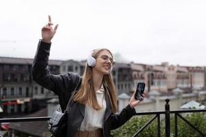 tanzende junge Frau in Kopfhörern mit einem Mobiltelefon vor dem Hintergrund eines Stadtpanoramas foto