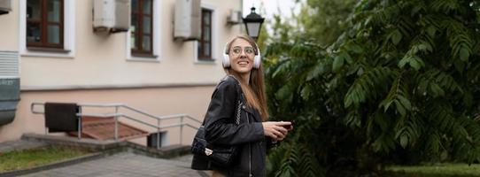 Porträt einer jungen Studentin in der Stadt in Kopfhörern mit einem Mobiltelefon foto