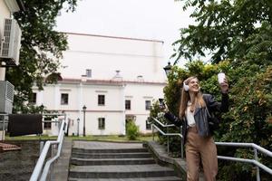 eine junge frau tanzt mit kopfhörern vor dem hintergrund der urbanen umgebung, ohne schüchtern zu sein foto