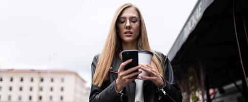 Porträt einer ernsthaften jungen Frau mit einer Tasse Kaffee, die auf ein Mobiltelefon blickt foto