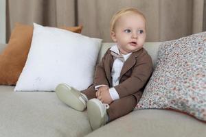 stylisches baby in businesskleidung sitzt auf der couch und schaut nach rechts foto