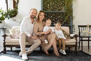 glückliche europäische familie mit zwei kleinen jungen kindern, die auf dem sofa im stilvollen zimmer sitzen foto