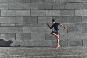 beste Ergebnisse erzielen. Volle Länge des jungen Mannes in Sportkleidung, der beim Training draußen läuft foto