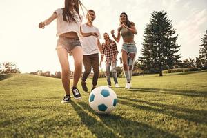 Gruppe junger lächelnder Menschen in Freizeitkleidung, die beim Fußballspielen im Freien laufen foto