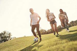 freundliche Konkurrenz. voller Länge von glücklichen jungen Menschen in Freizeitkleidung, die beim Fußballspielen im Freien laufen foto