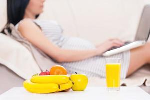 schwangere Frau mit Laptop. Schöne schwangere Frau, die am Laptop arbeitet, während sie auf einer Couch liegt foto