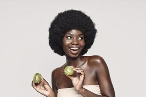 porträt einer schönen jungen afrikanischen frau, die stücke von kiwi hält und lächelt foto