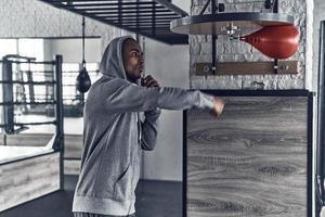 Er ist ein neuer Champion. hübscher junger afrikanischer mann in sportkleidung boxt beim training im fitnessstudio foto