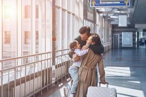 glückliche Familie, die sich umarmt und lächelt, während sie sich am Flughafenterminal wiedervereint foto