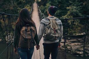 nächsten Schritt machen. Rückansicht des jungen Paares, das beim gemeinsamen Wandern im Wald auf die Hängebrücke tritt foto