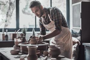 selbstbewusster und inspirierter Töpfer. Selbstbewusster junger Mann, der Keramiktopf auf der Töpferscheibe herstellt foto