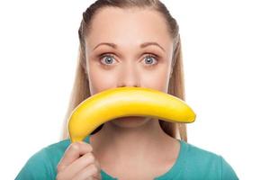 Frau mit Banane. schöne junge frau, die banane vor ihrem gesicht hält und positivität ausdrückt, während sie isoliert auf weiß steht foto