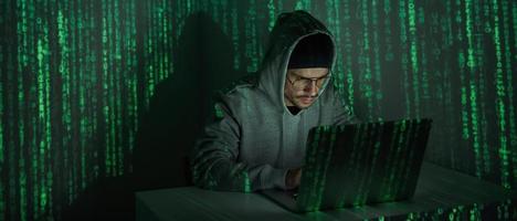 Selbstbewusster junger Mann im Kapuzenhemd mit Computer vor dunklem Hintergrund foto