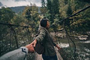 echtes Vertrauen. schöne junge frau, die hände mit ihrem freund hält, während sie auf der hängebrücke geht foto