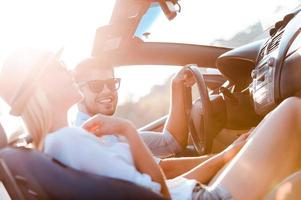 der beste Tag für den Roadtrip. glückliches junges Paar lächelt, während es in seinem Cabrio sitzt foto