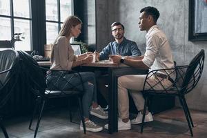 gruppe junger leute in eleganter freizeitkleidung, die während der arbeit im büro über geschäfte diskutieren foto