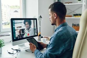 hübscher junger mann, der im büro per videoanruf mit kollegen spricht foto