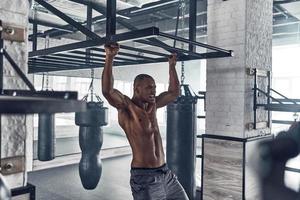 alles ist möglich. hübscher junger afrikaner, der beim training im fitnessstudio Klimmzüge macht foto