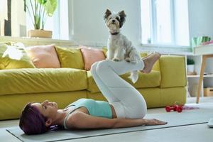 junge frau in sportkleidung, die zu hause mit ihrem kleinen hund trainiert foto